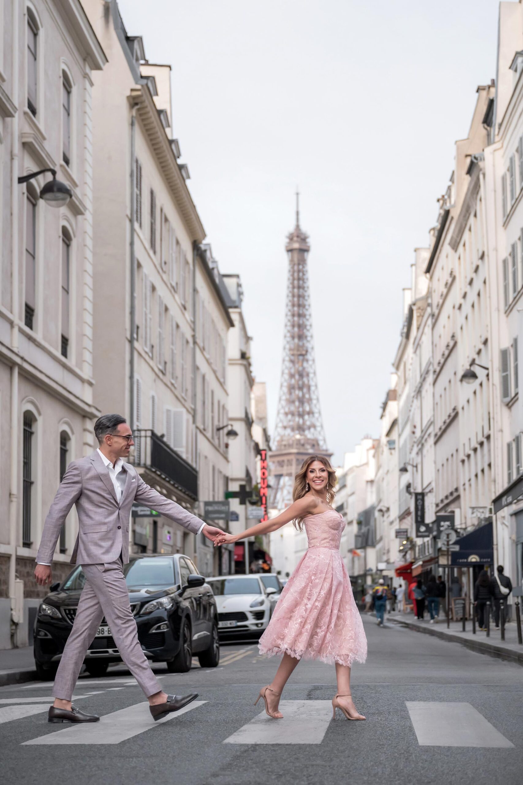 Couple crossing Paris street holding hands with Eiffel Tower during photoshoot